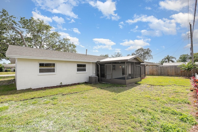 rear view of house with central AC unit, a sunroom, fence, a yard, and concrete block siding