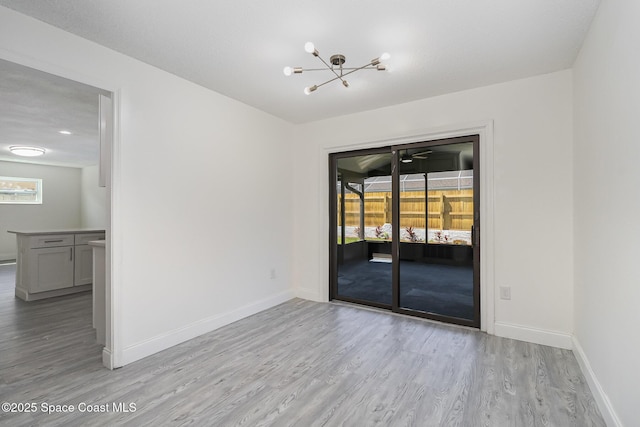 spare room featuring baseboards, light wood-style flooring, a chandelier, and a wealth of natural light