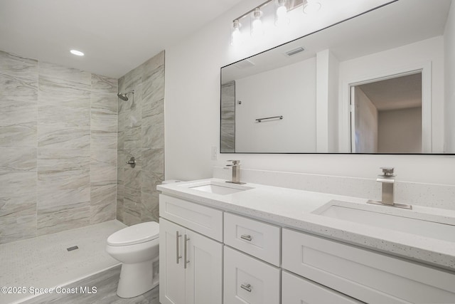 bathroom with visible vents, a sink, a tile shower, and toilet