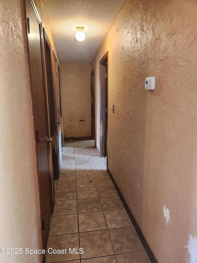 hallway with tile patterned floors, a textured wall, and a textured ceiling
