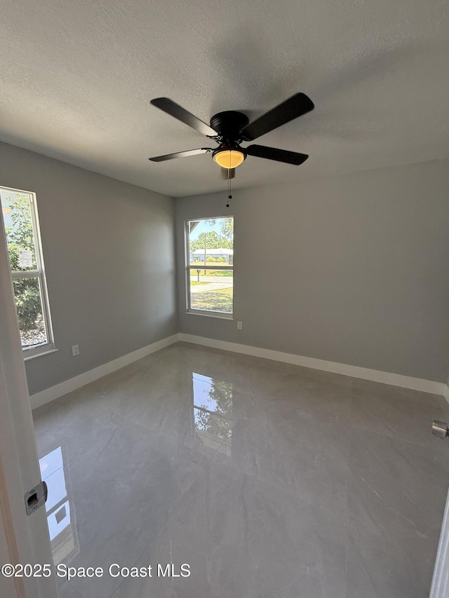 empty room featuring baseboards, a ceiling fan, and a textured ceiling