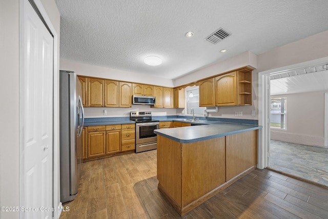 kitchen featuring a textured ceiling, visible vents, appliances with stainless steel finishes, wood finished floors, and a peninsula