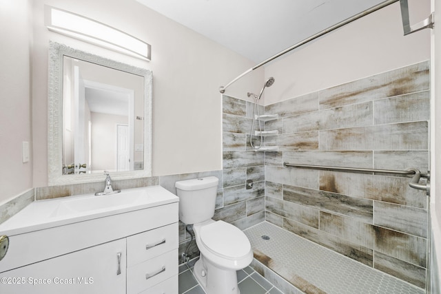 bathroom with a tile shower, tile patterned flooring, vanity, toilet, and tile walls