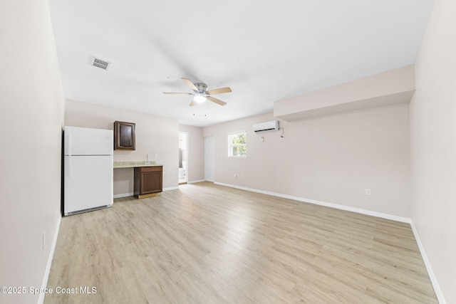 unfurnished living room with visible vents, a ceiling fan, light wood-style floors, and a wall mounted AC