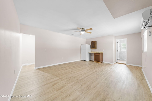 unfurnished living room featuring baseboards, a ceiling fan, light wood finished floors, and a wall mounted air conditioner
