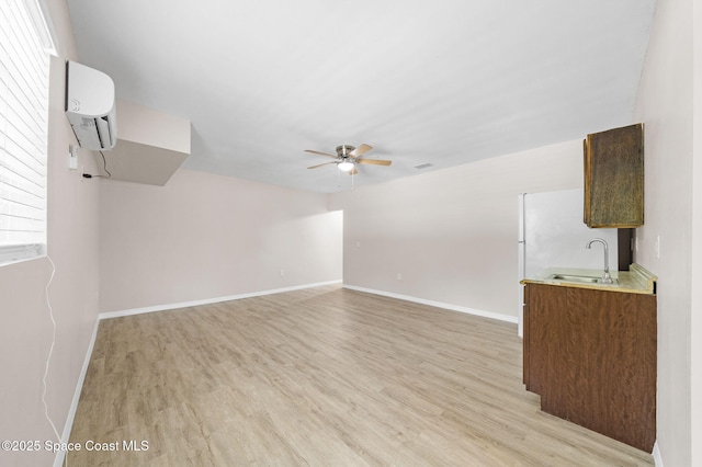 unfurnished living room with ceiling fan, a wall mounted AC, a sink, baseboards, and light wood-style floors
