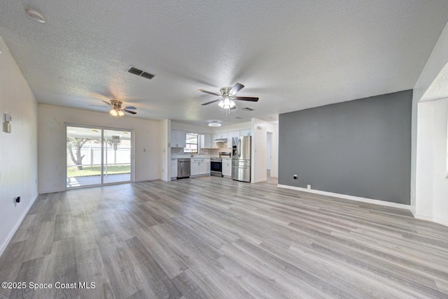 unfurnished living room featuring visible vents, baseboards, a textured ceiling, a ceiling fan, and light wood-style flooring