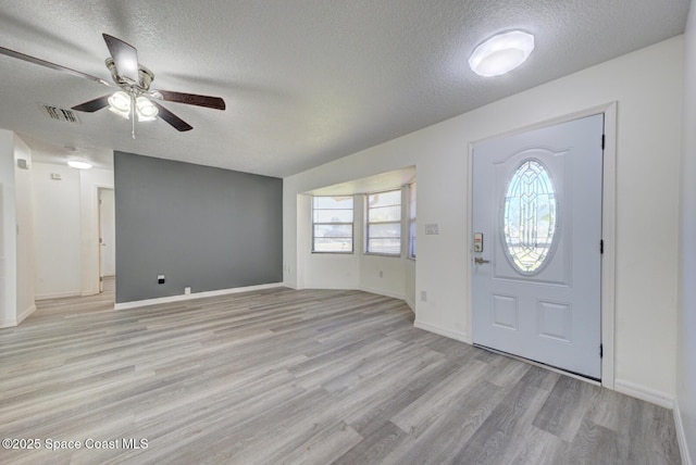 foyer entrance featuring visible vents, baseboards, ceiling fan, light wood-type flooring, and a textured ceiling