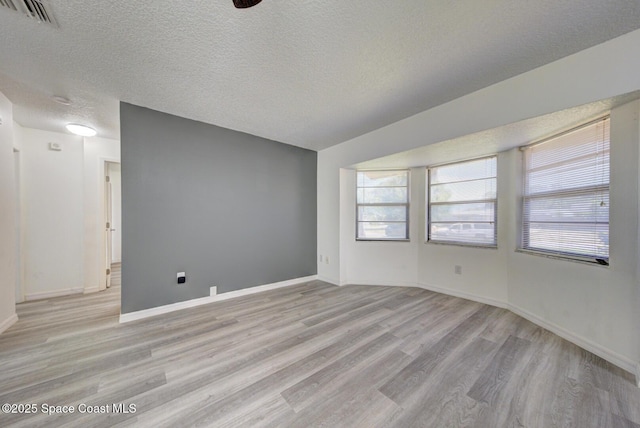 unfurnished room with baseboards, light wood finished floors, a textured ceiling, and visible vents