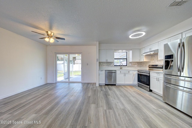 kitchen featuring appliances with stainless steel finishes, a sink, open floor plan, under cabinet range hood, and visible vents