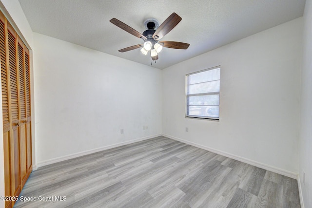 unfurnished bedroom featuring a closet, baseboards, a textured ceiling, a ceiling fan, and light wood finished floors