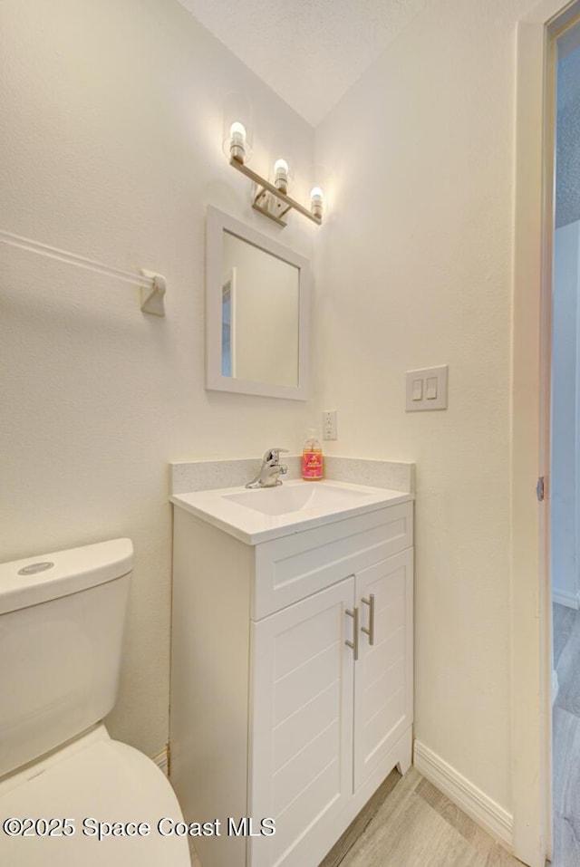 bathroom with vanity, baseboards, wood finished floors, and toilet