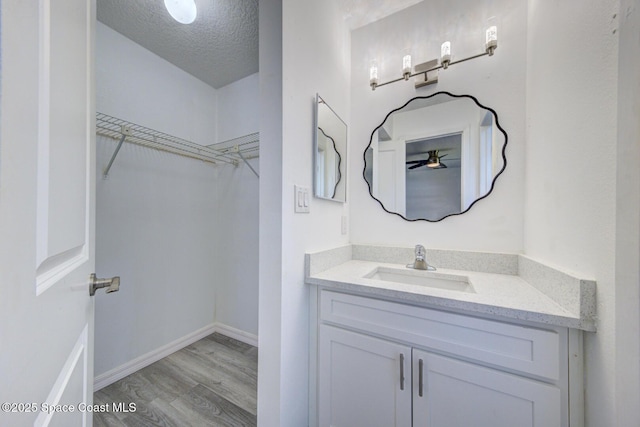 bathroom with a walk in closet, a textured ceiling, wood finished floors, baseboards, and vanity