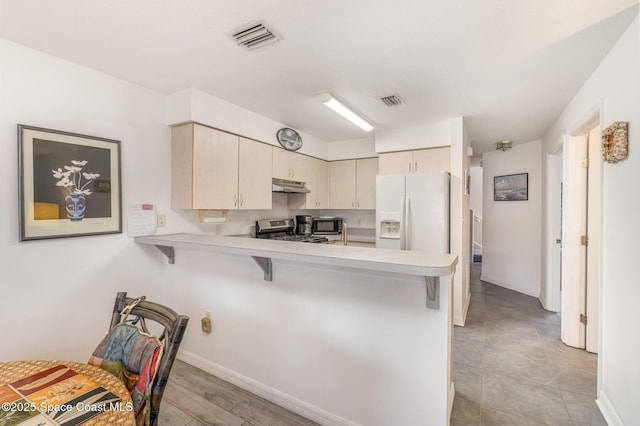 kitchen with light countertops, a peninsula, under cabinet range hood, visible vents, and stainless steel range oven