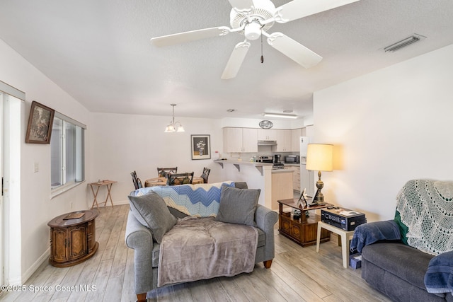 living room featuring baseboards, visible vents, ceiling fan with notable chandelier, and light wood-style floors