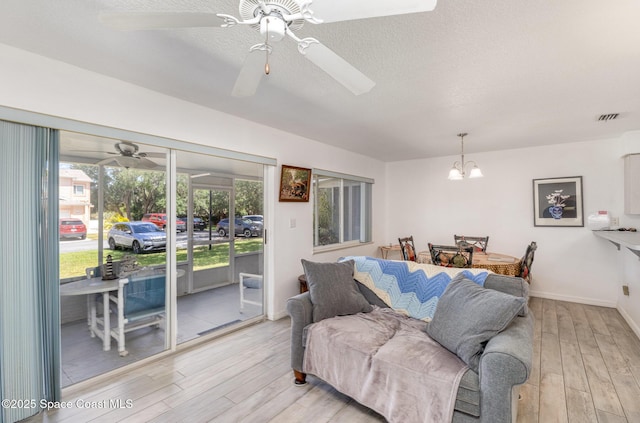 living area featuring visible vents, a textured ceiling, light wood finished floors, and ceiling fan with notable chandelier
