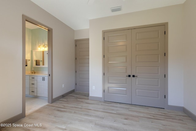unfurnished bedroom featuring light wood finished floors, baseboards, ensuite bathroom, visible vents, and a closet