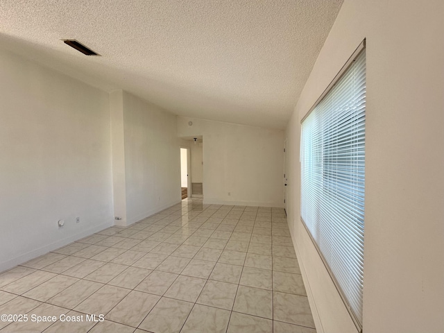 empty room featuring light tile patterned flooring, a textured ceiling, visible vents, and lofted ceiling