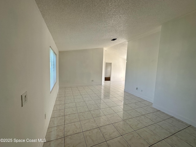 empty room with light tile patterned floors, baseboards, and a textured ceiling