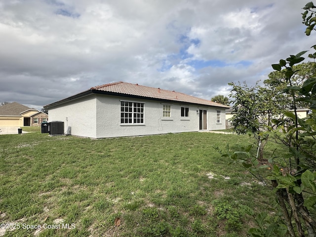 rear view of property featuring central air condition unit, a tiled roof, a lawn, and stucco siding