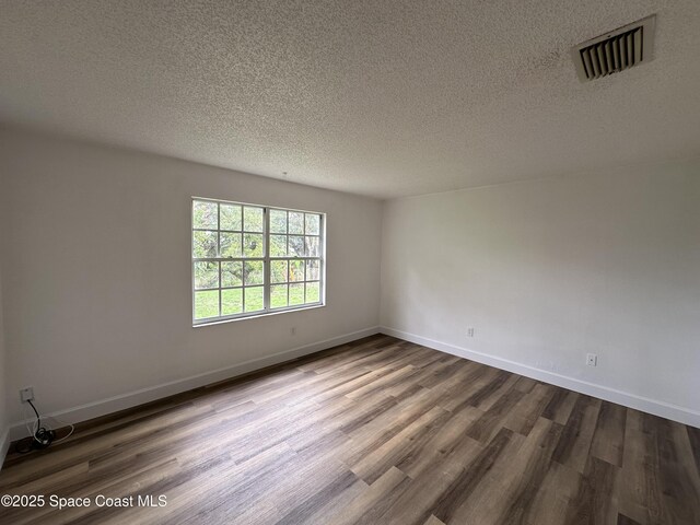 spare room featuring baseboards, dark wood-style floors, a textured ceiling, and visible vents
