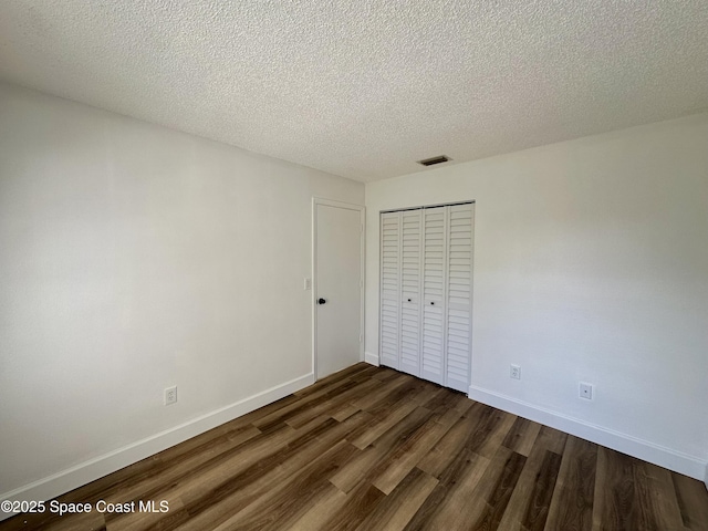 unfurnished bedroom with a textured ceiling, baseboards, visible vents, dark wood-style floors, and a closet