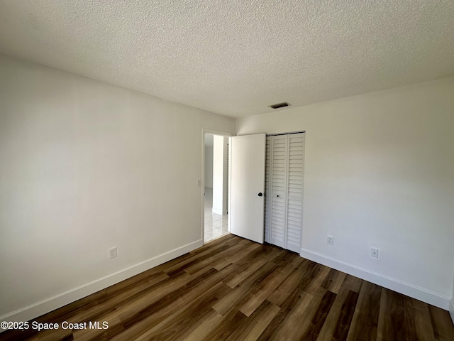 unfurnished bedroom featuring visible vents, a closet, baseboards, dark wood-type flooring, and a textured ceiling