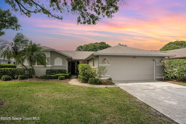 ranch-style home with a garage, a front lawn, stucco siding, a shingled roof, and concrete driveway