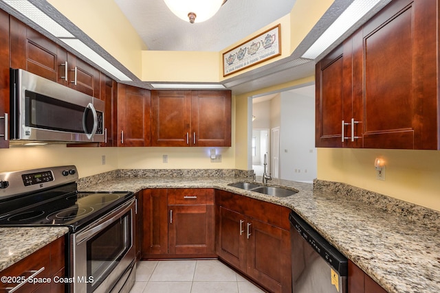 kitchen featuring stainless steel appliances, light tile patterned floors, a sink, and light stone counters