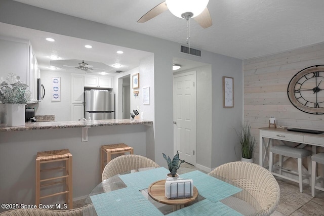 dining space with visible vents, baseboards, ceiling fan, wooden walls, and recessed lighting