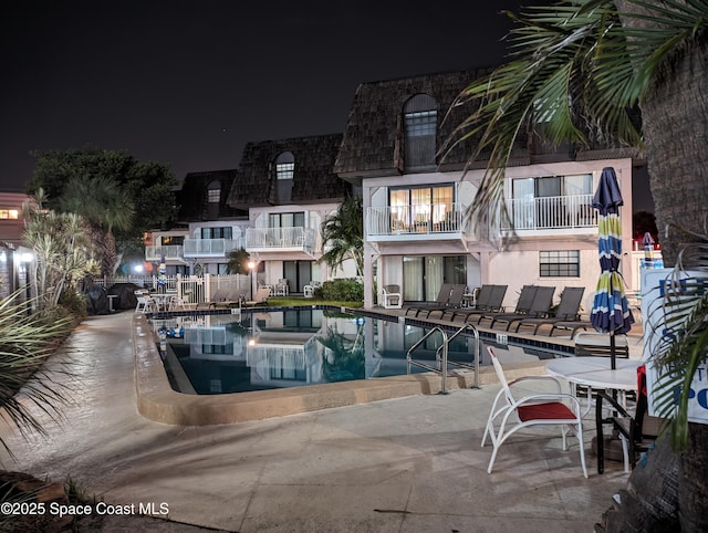pool at night featuring a community pool and a patio area