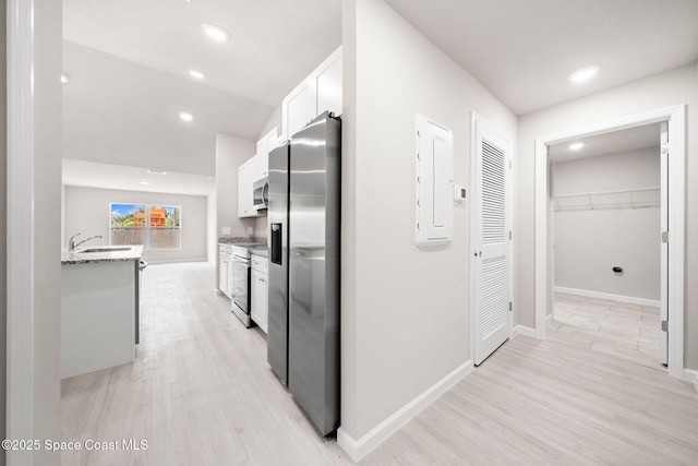 corridor featuring baseboards, a sink, light wood finished floors, and recessed lighting