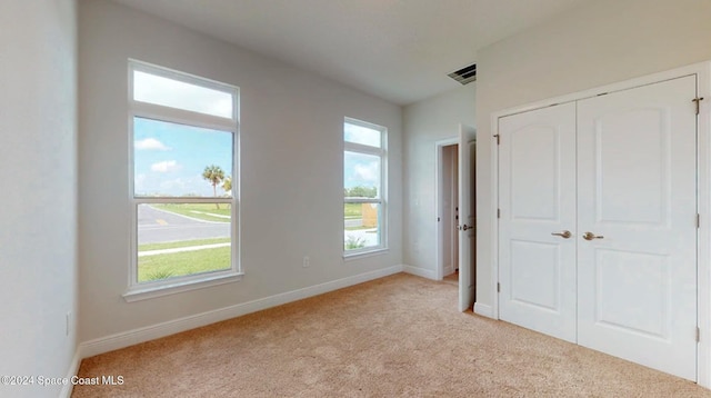 unfurnished bedroom featuring baseboards, light carpet, a closet, and visible vents