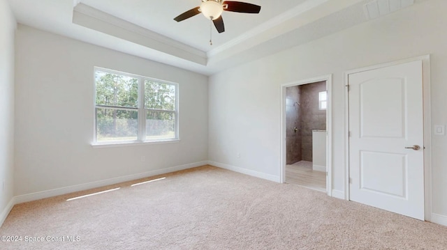 unfurnished bedroom featuring connected bathroom, light colored carpet, baseboards, a tray ceiling, and ornamental molding