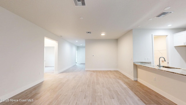 unfurnished living room featuring visible vents, a sink, and light wood-type flooring
