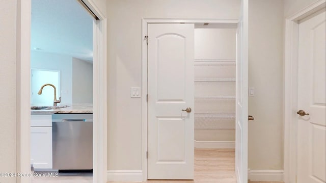hall with light wood-type flooring, a sink, and baseboards