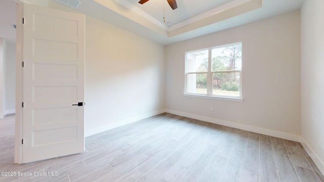 spare room featuring baseboards, light wood-style floors, ceiling fan, and a tray ceiling