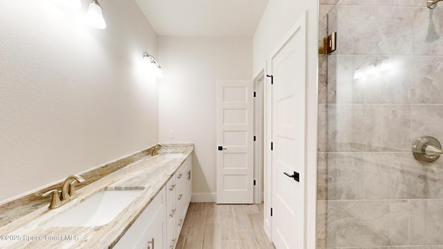 bathroom featuring double vanity, a tile shower, wood finish floors, a sink, and baseboards