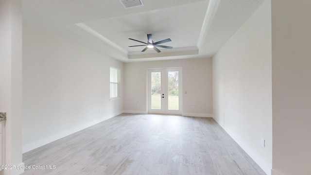 empty room featuring ceiling fan, visible vents, baseboards, a tray ceiling, and light wood-style flooring