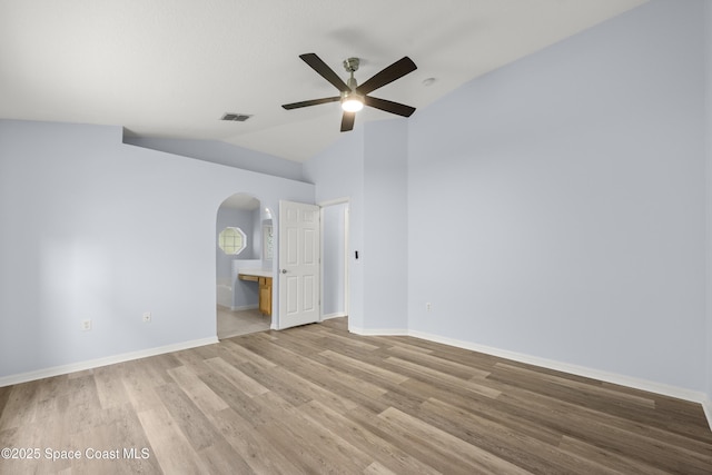 unfurnished room with visible vents, a ceiling fan, light wood-type flooring, arched walkways, and vaulted ceiling