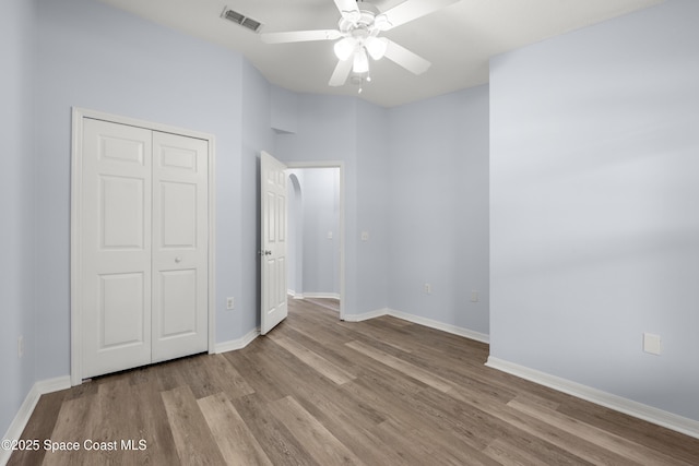 unfurnished bedroom with visible vents, a closet, wood finished floors, baseboards, and a ceiling fan