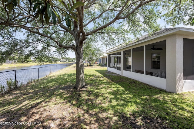 view of yard featuring a water view, fence, ceiling fan, and a sunroom