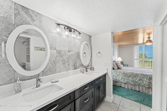 ensuite bathroom with tile patterned floors, double vanity, and a textured ceiling