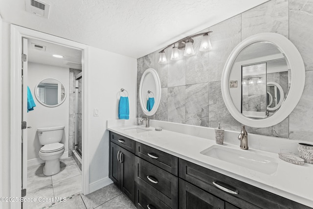 full bath with toilet, double vanity, a stall shower, a textured ceiling, and baseboards