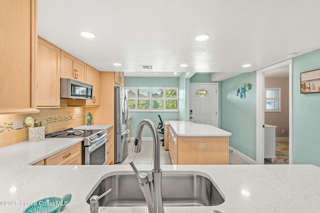 kitchen with appliances with stainless steel finishes, a sink, light brown cabinets, a kitchen island, and baseboards