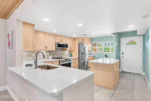 kitchen with appliances with stainless steel finishes, a sink, light brown cabinets, a center island, and tasteful backsplash