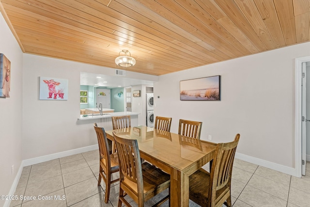 dining room featuring stacked washing machine and dryer, wooden ceiling, light tile patterned floors, and baseboards