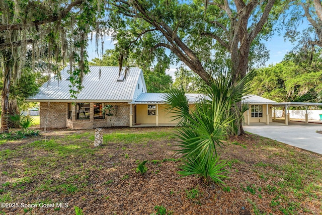 view of front facade featuring covered porch, metal roof, a detached carport, brick siding, and concrete driveway