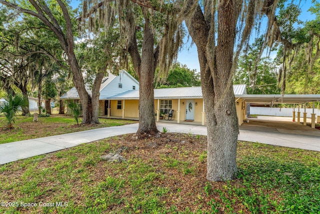 view of front of house featuring covered porch, driveway, metal roof, a carport, and stucco siding