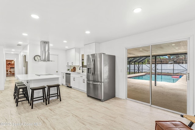 kitchen featuring appliances with stainless steel finishes, a sink, white cabinetry, island range hood, and a kitchen bar